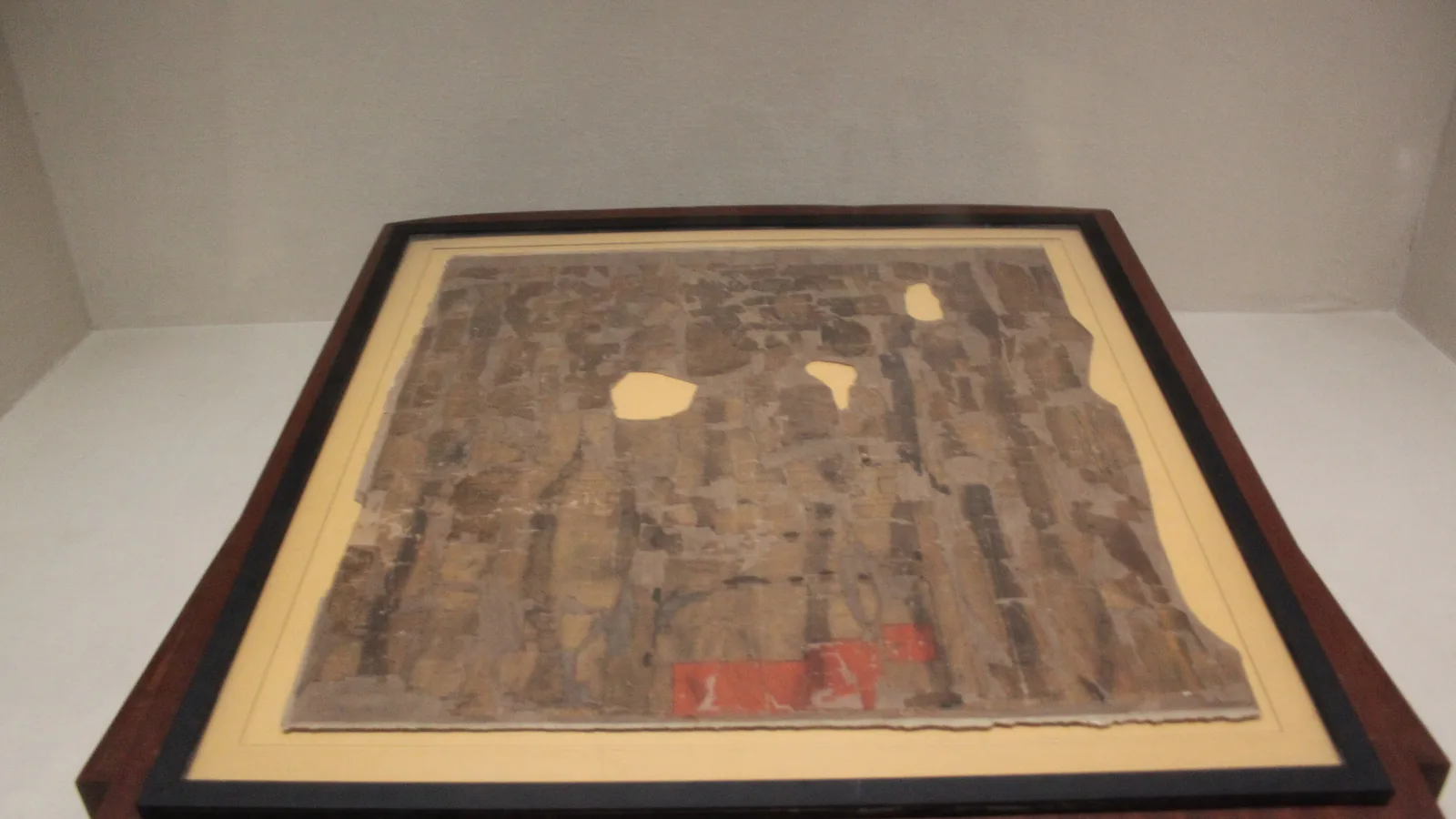 Fragmentary silk map with faint ink lines and red marks, mounted and lit in a museum display case