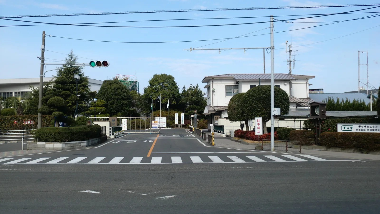 The main gate of a chemical factory with a gatehouse, a signboard and industrial buildings behind it