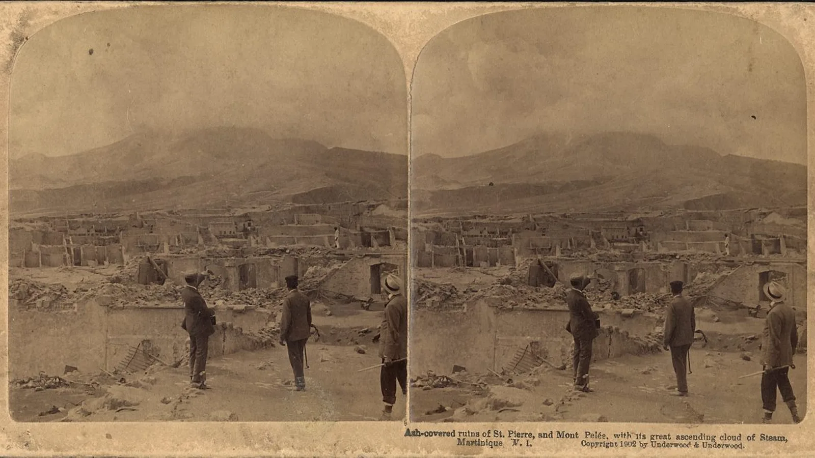 Black-and-white stereo photograph of men standing among ash-covered ruined walls with the volcano and its steam cloud behind