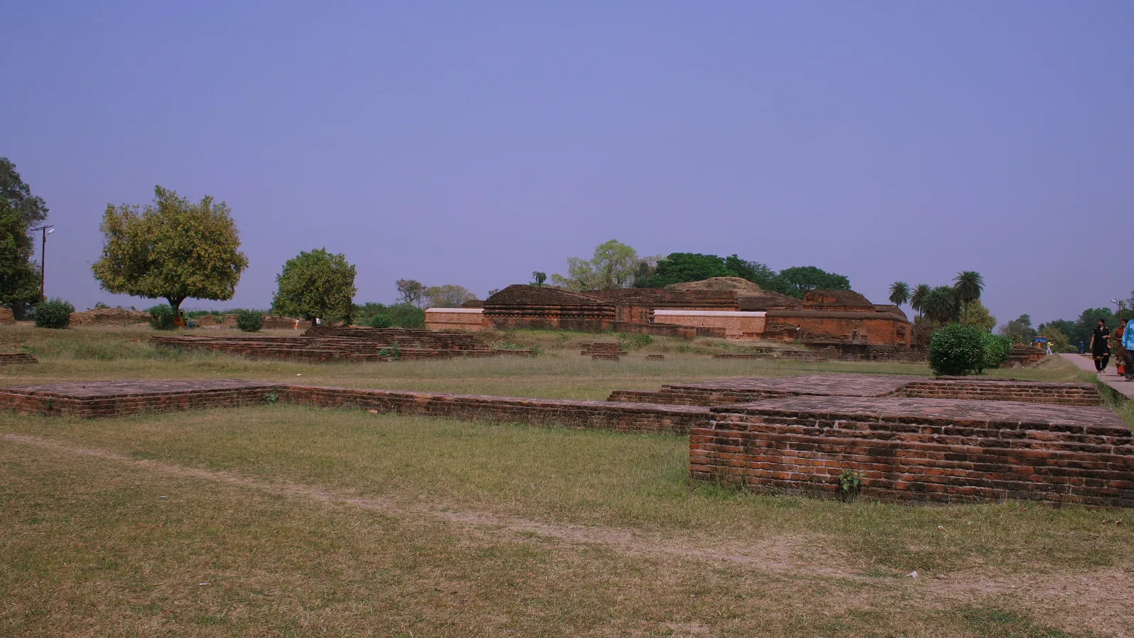 Low brick foundation walls of excavated monastery cells at Nalanda with mounds beyond