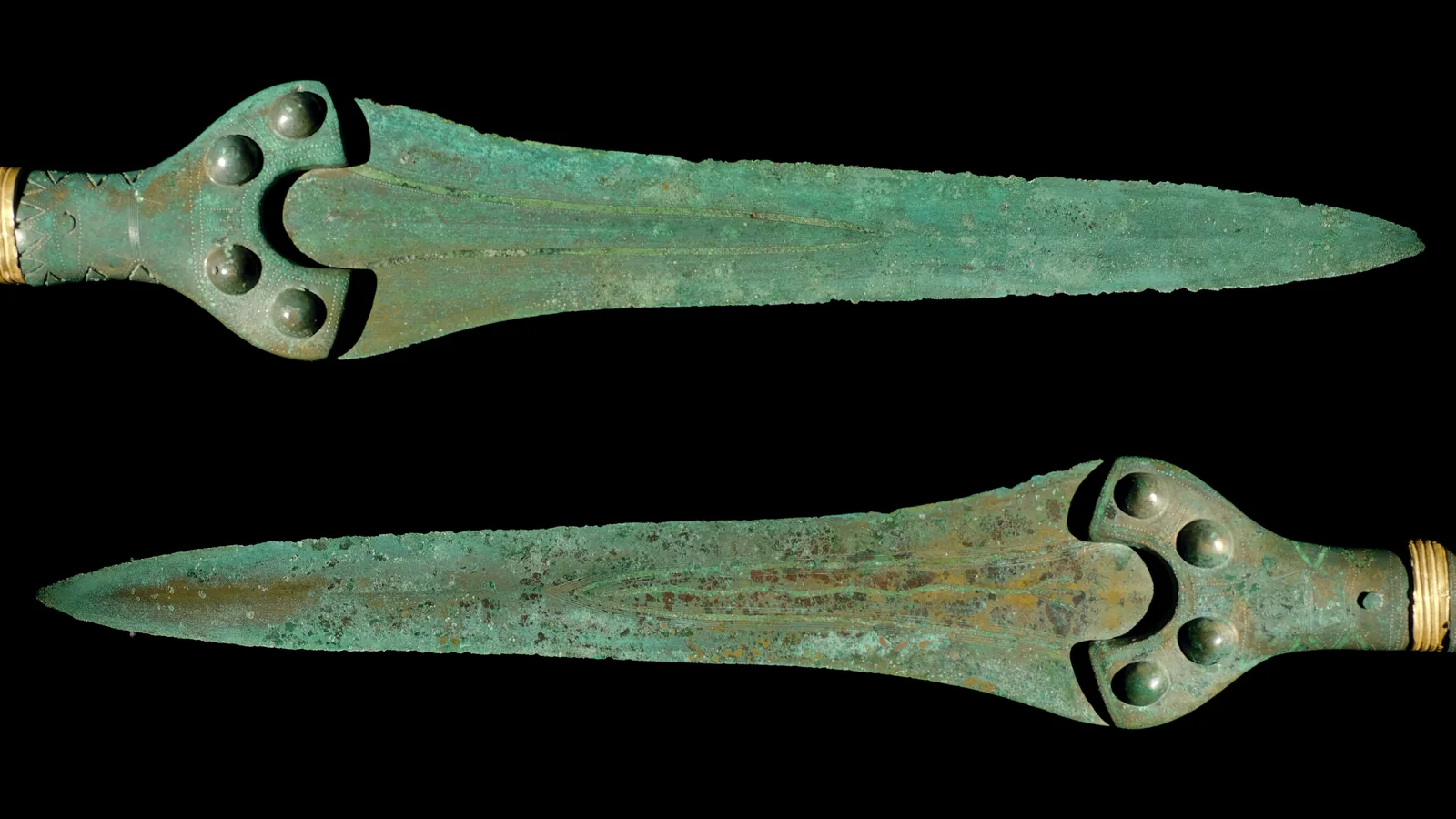 Two bronze swords with gold-banded hilts lying side by side on a dark background
