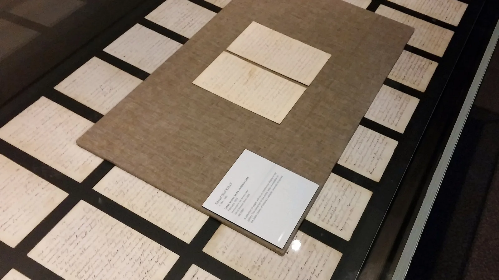 small handwritten pages laid out in a glass display case with a printed label