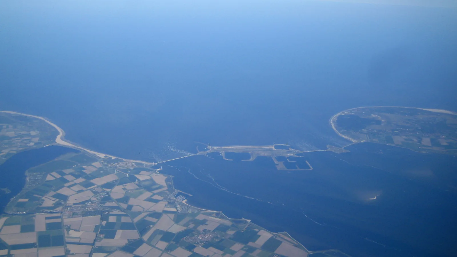 Aerial view of a long storm surge barrier of piers and gates spanning a sea inlet between two shores