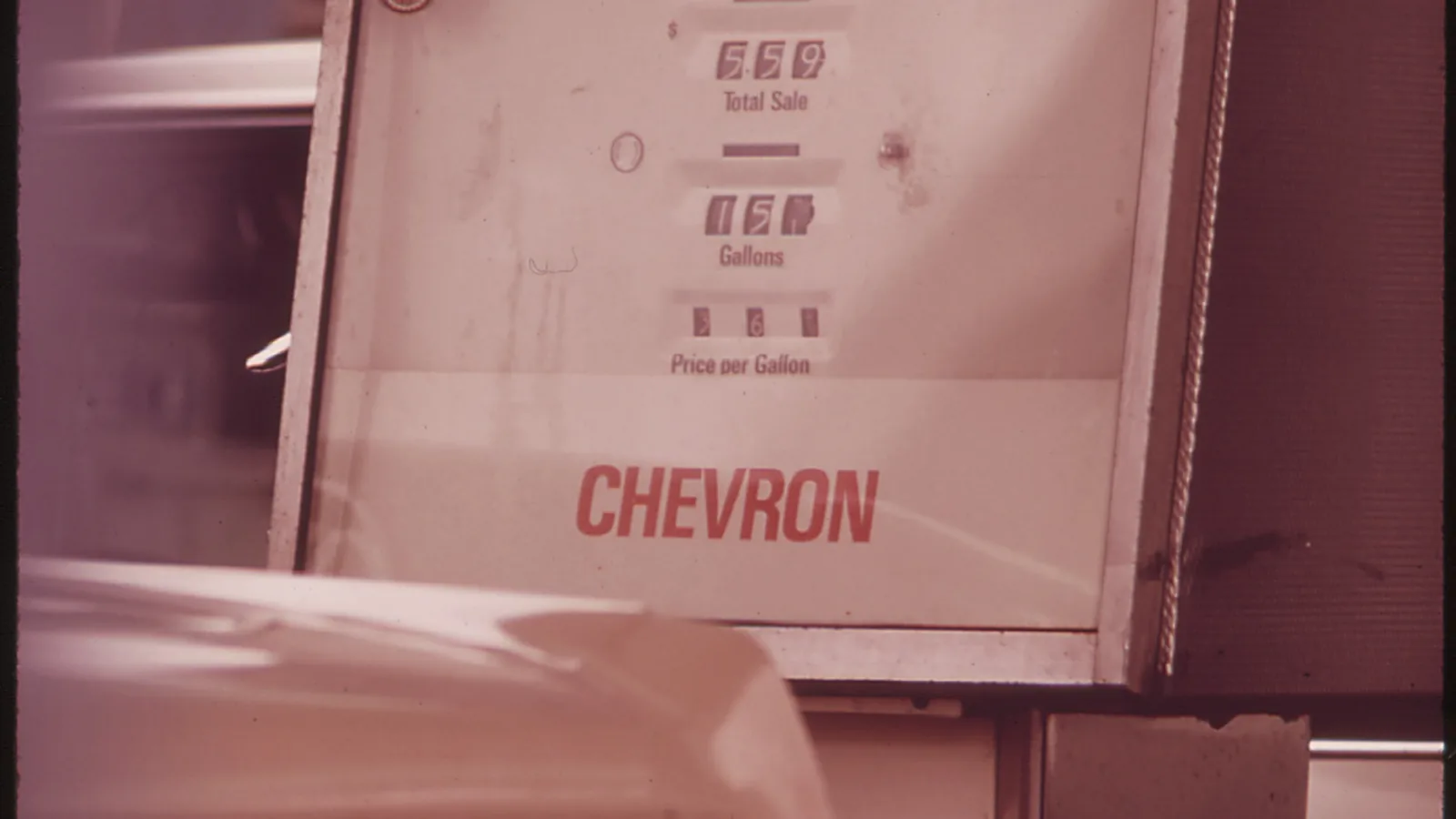 a close view of a gasoline pump with dials for total sale, gallons and price per gallon, a 1970s color photograph