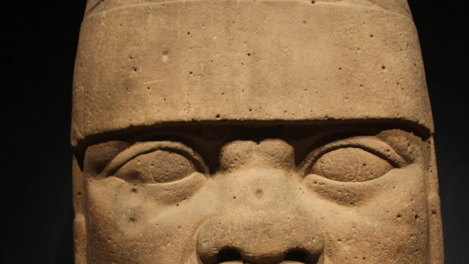 a massive carved basalt head with a broad face, thick lips and a close-fitting helmet, seen from the front