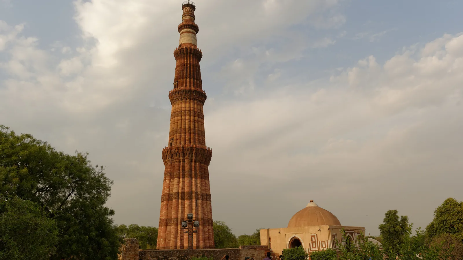 The fluted red sandstone tower of the Qutb Minar beside a domed gateway, Delhi