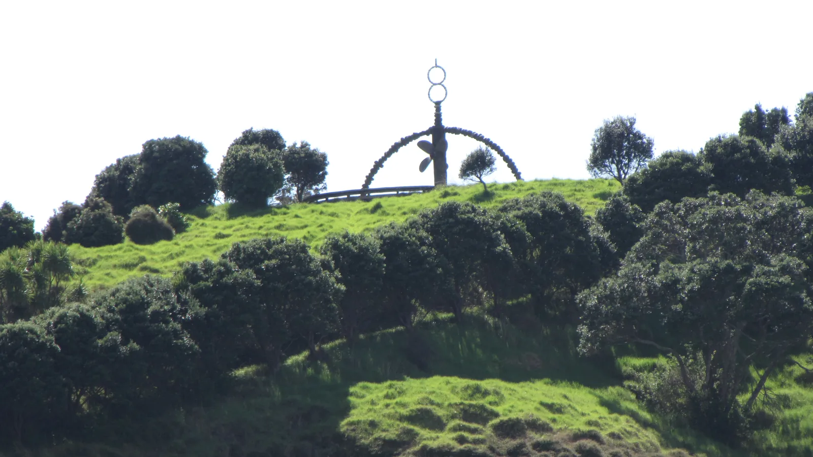 A stone arch sculpture on a grassy hilltop overlooking a bay and offshore islands