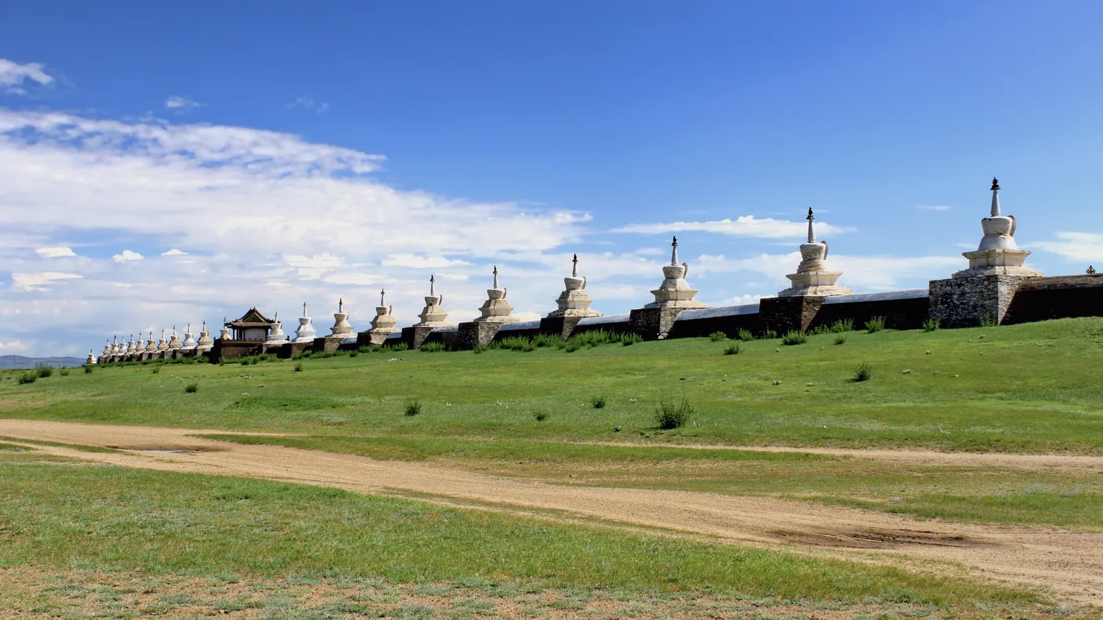 A long whitewashed wall lined with white stupas stretching across open grassland