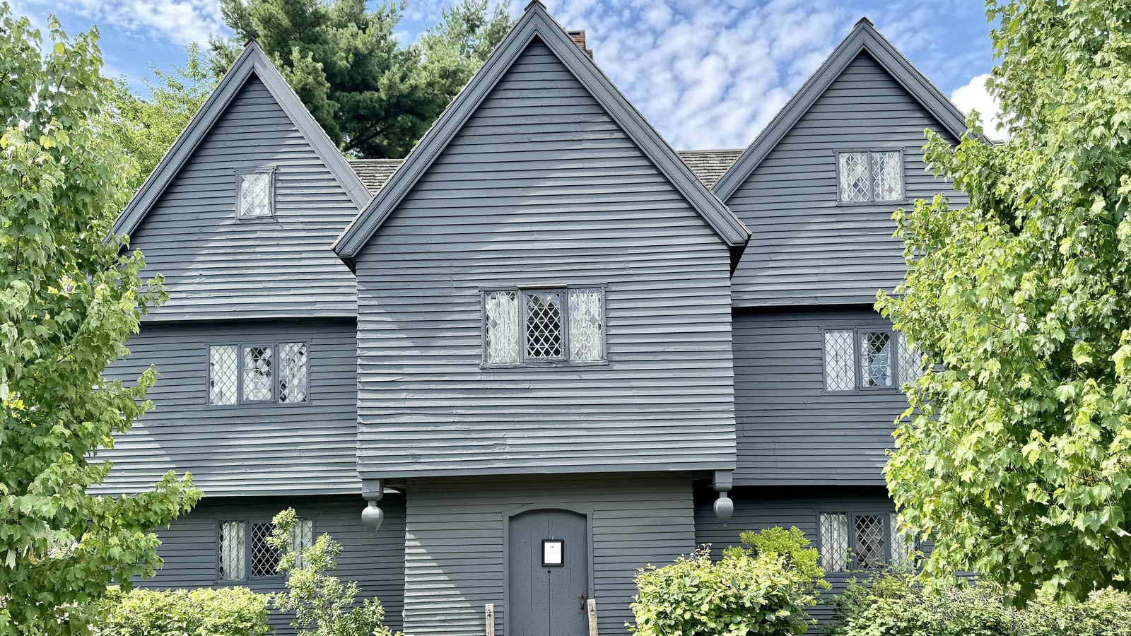 Dark timber-framed colonial house with steep gables and diamond-pane windows on a street corner
