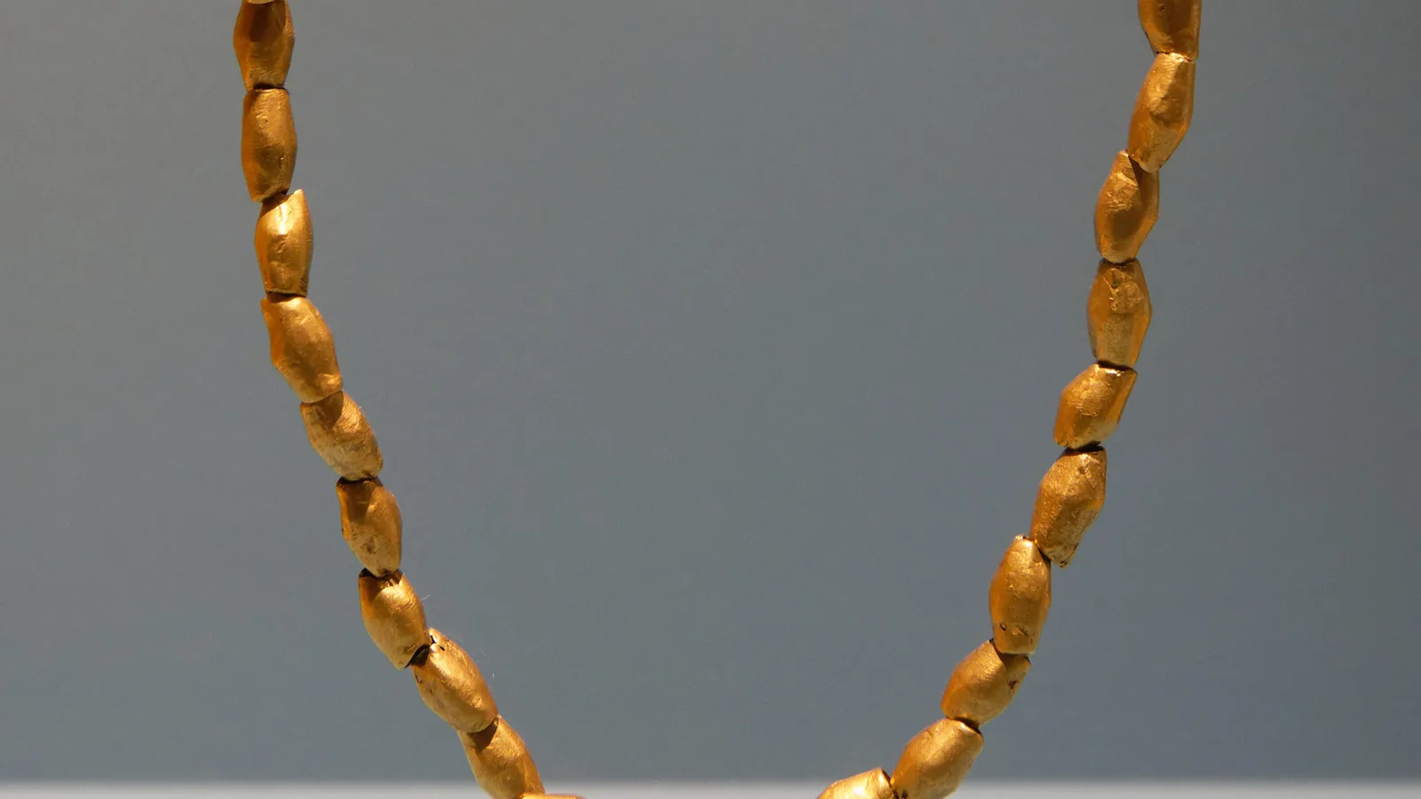 Necklace of gold beads from Sarazm displayed on a grey background