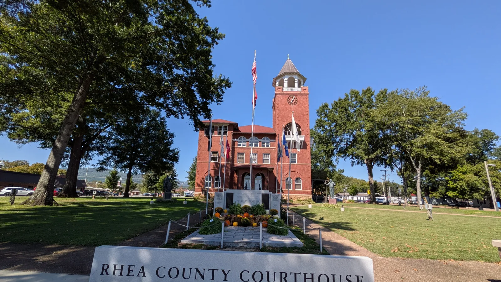 a red brick courthouse with a clock tower behind trees and a stone sign reading Rhea County Courthouse