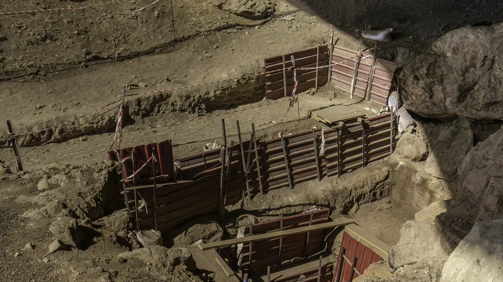 A deep rectangular excavation trench with stepped earth walls inside a large cave