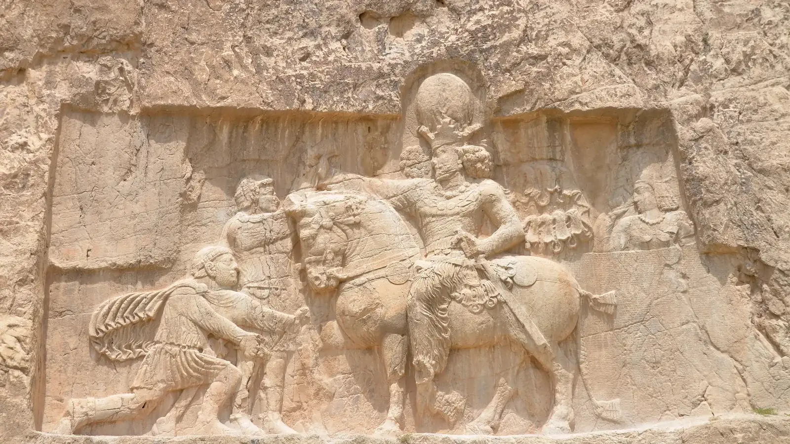a rock relief of a mounted king facing two Roman figures, one kneeling