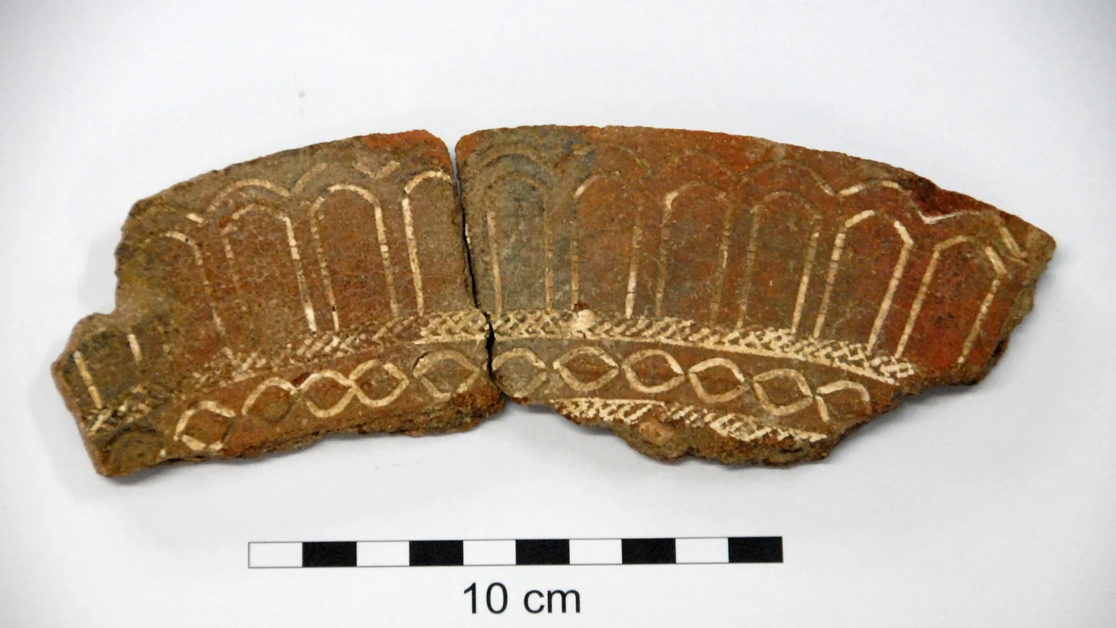 Fragment of a reddish pot rim covered in rows of fine stamped dots filled with white lime