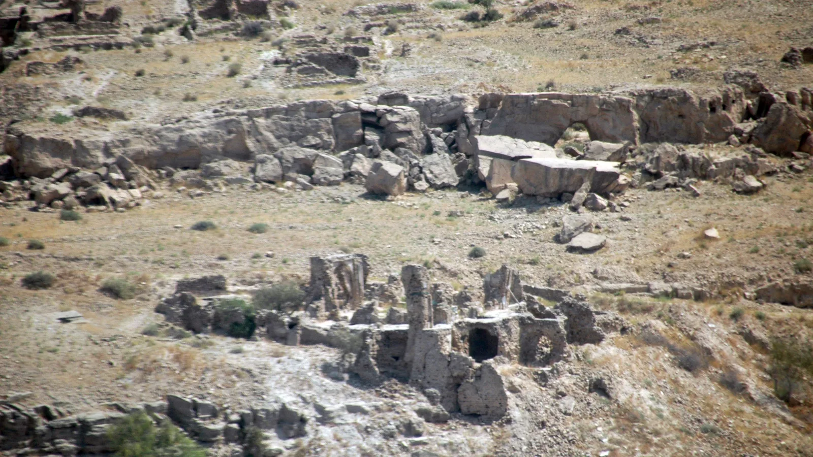Weathered stone and mud-brick ruins scattered across a dry, rocky hillside