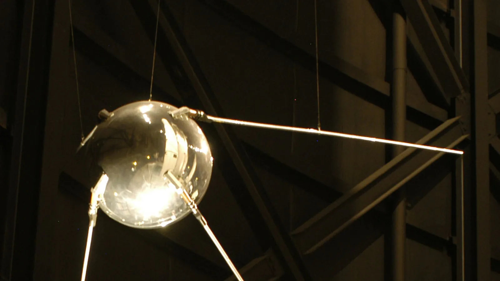 a polished metal sphere with four long antennas, photographed against a dark background