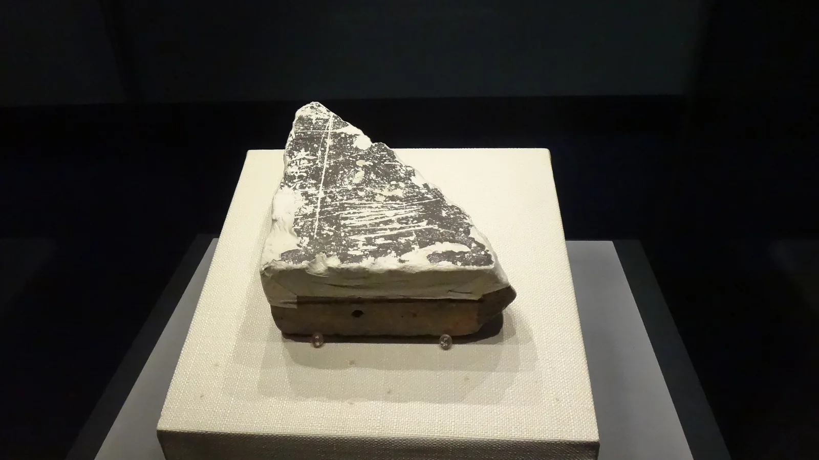 Museum display of a broken ceramic brick fragment inscribed with an incised year mark, mounted on a stand
