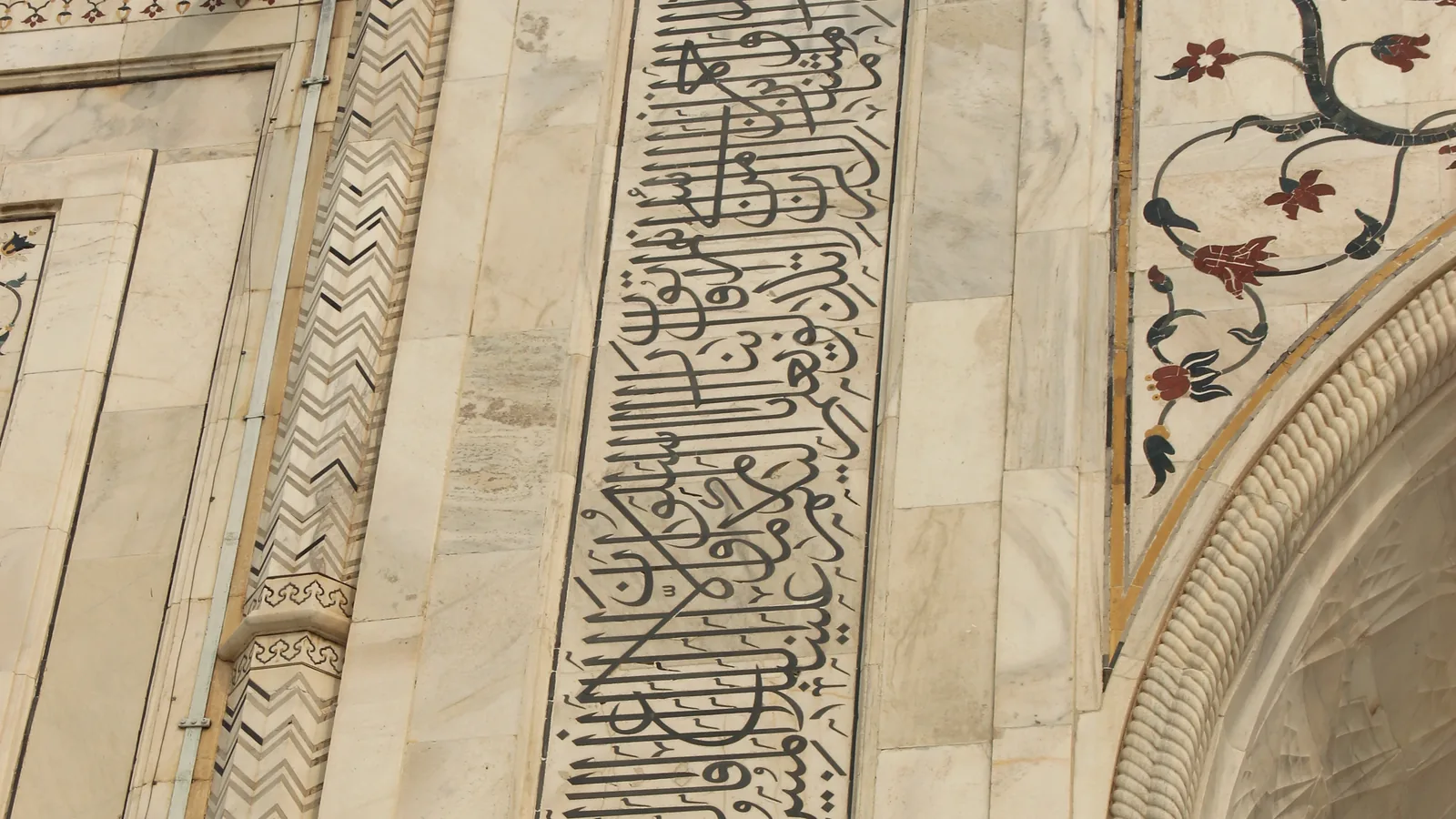 a tall band of black inlaid Arabic calligraphy framing a marble archway, with inlaid flowers beside it