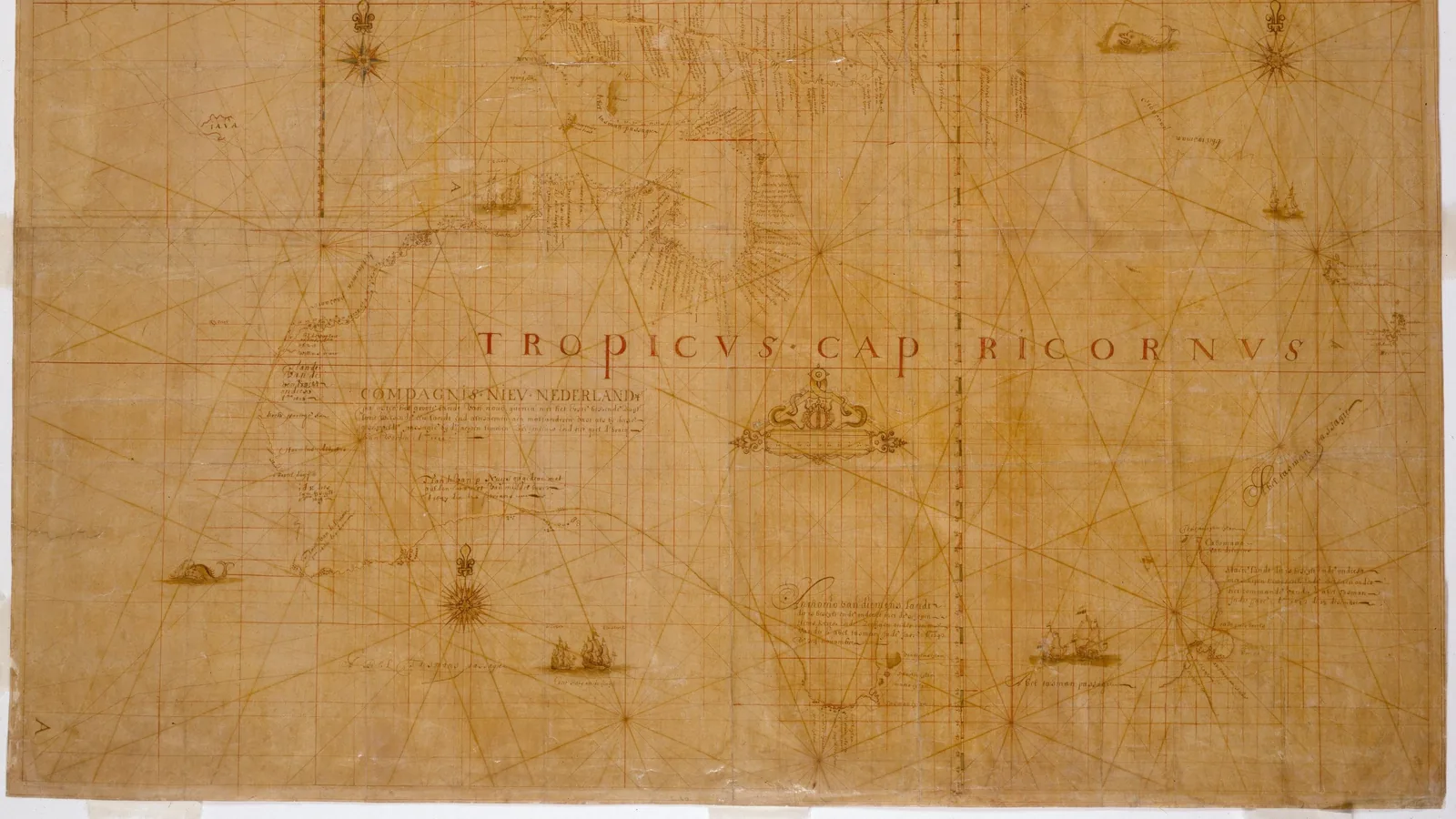 the lower part of a faded manuscript chart with a coastline, rhumb lines and small drawings of ships
