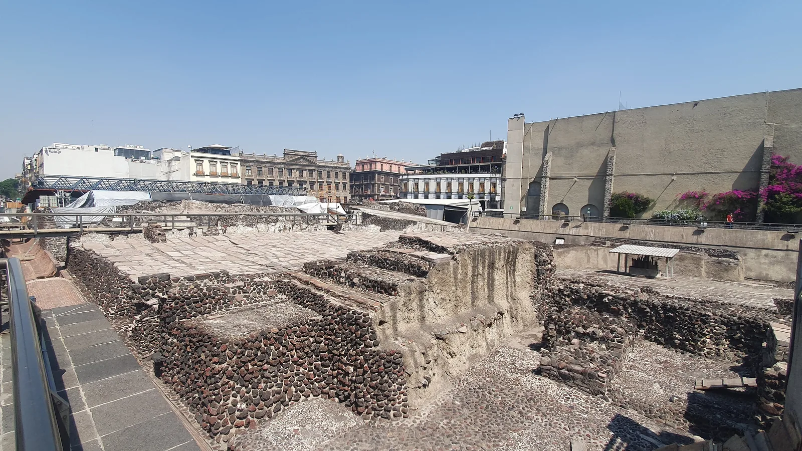 Excavated stone foundations of the Templo Mayor's eastern precinct beside modern Mexico City buildings
