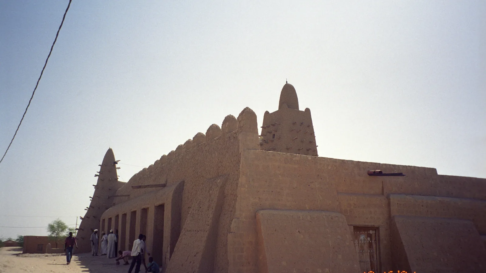 a mud-brick mosque with a tapering tower studded with projecting timber beams, under a pale sky