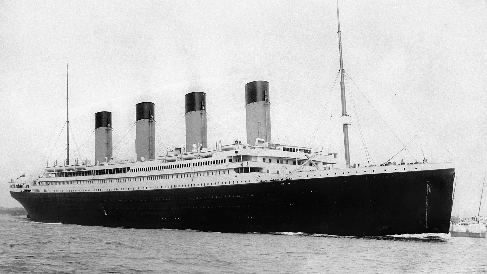 Large four-funnel ocean liner departing a harbor with smoke rising from its funnels