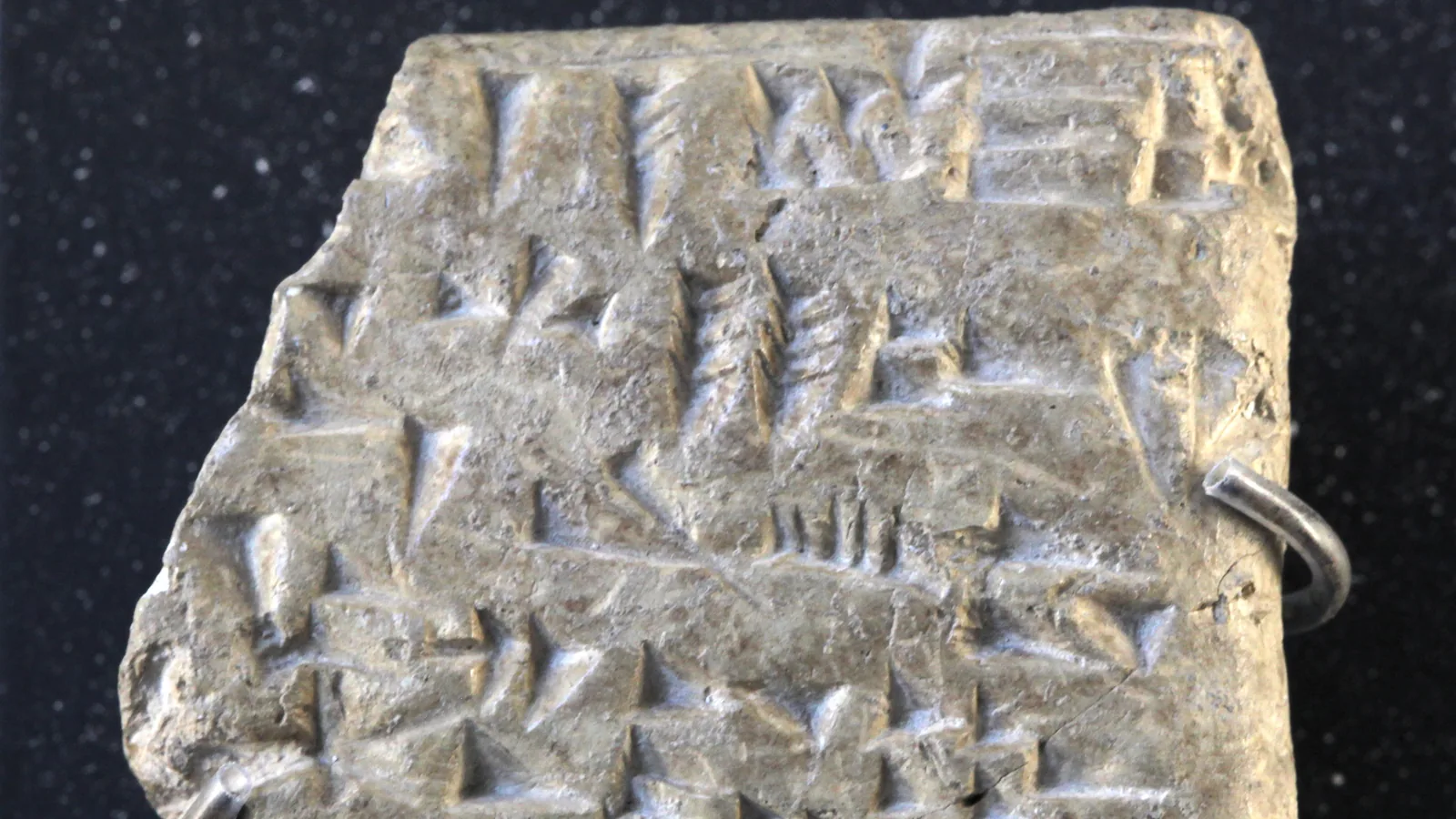 a small square clay tablet with rows of wedge-shaped cuneiform signs, on a museum stand