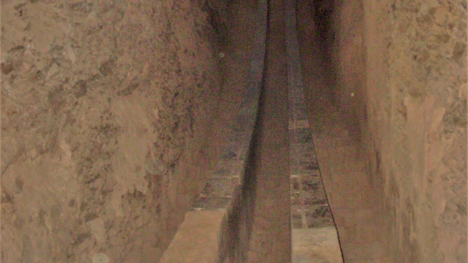 a narrow stone-lined trench cut into rock, with two curved marble rails running down its centre into shadow
