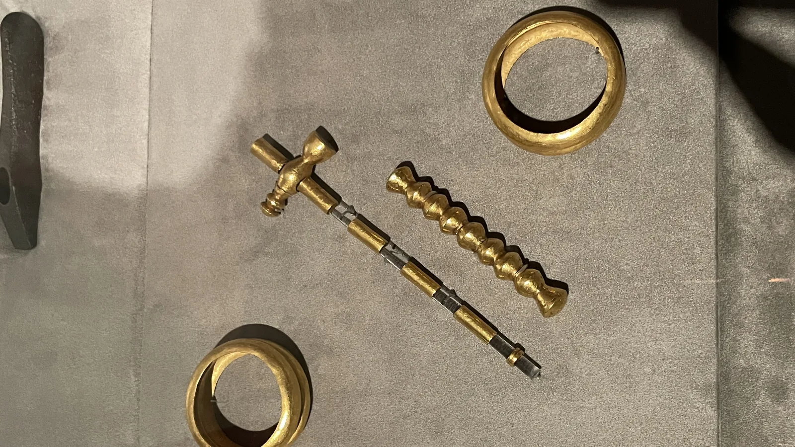 Two gold bracelets and a gold-sheathed ceremonial pin or scepter in a museum display case