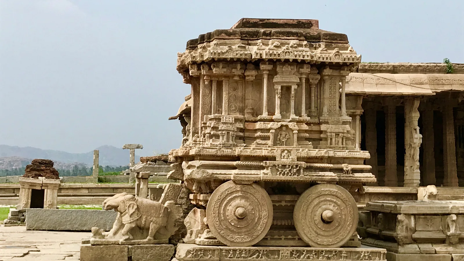 A stone shrine carved to resemble a wheeled chariot, standing in a temple courtyard at Hampi