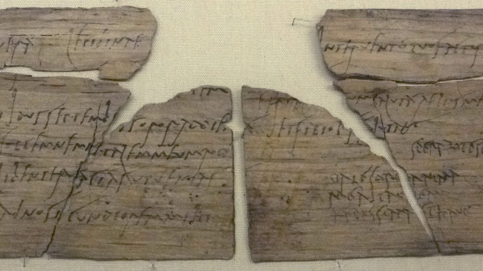 Fragments of a thin wooden leaf tablet with faint handwritten ink lines of Latin cursive script