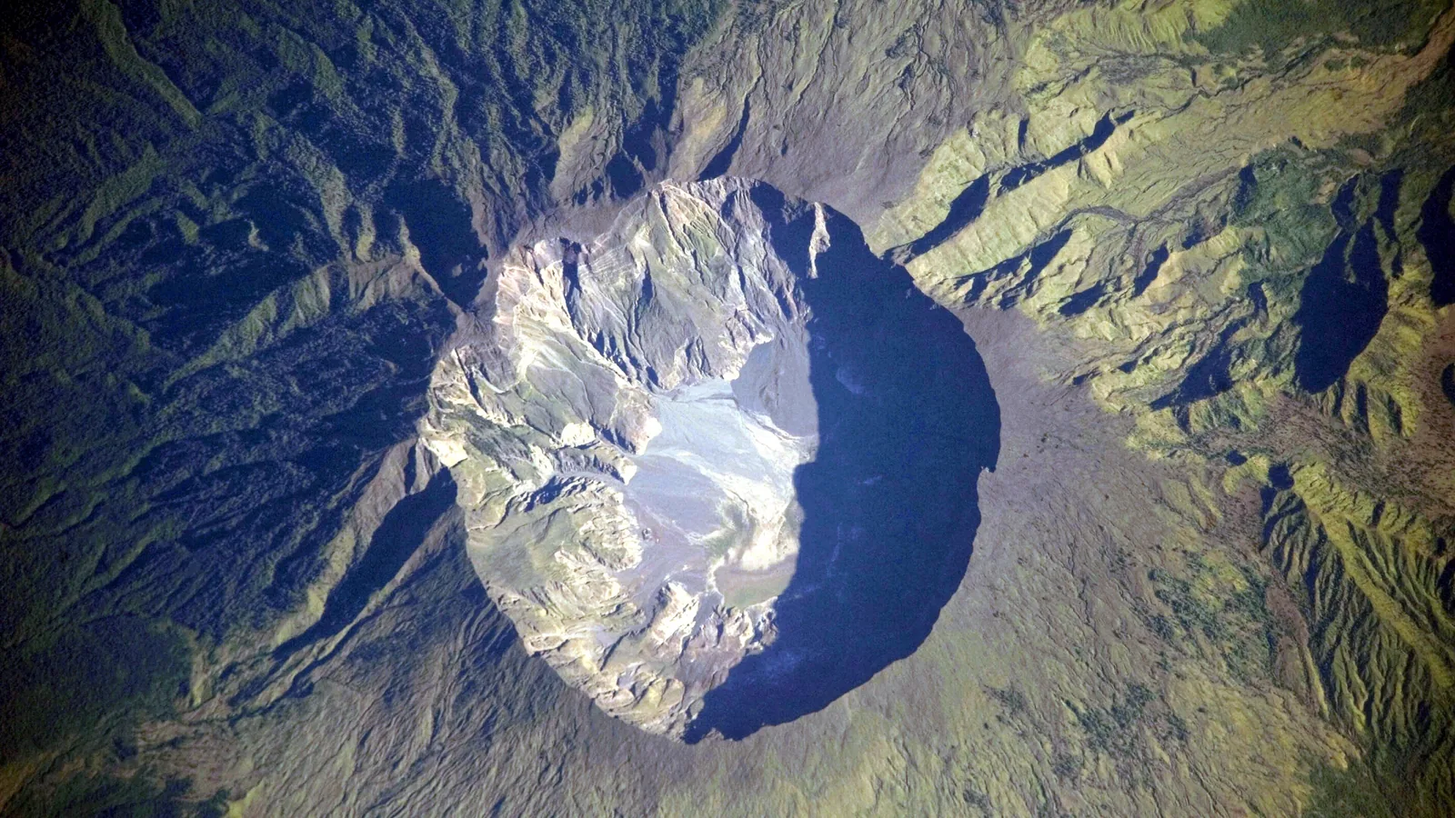 Astronaut photograph looking down into the huge round caldera of Tambora, ringed by green forested slopes